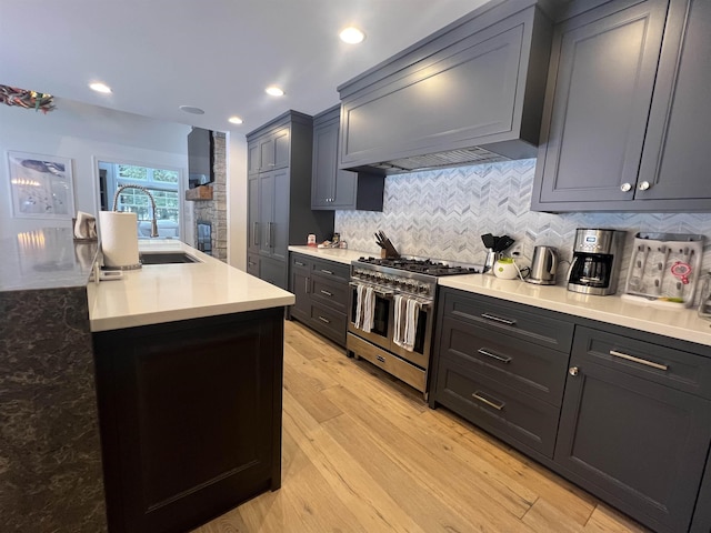 kitchen with custom exhaust hood, range with two ovens, a sink, decorative backsplash, and light wood-type flooring