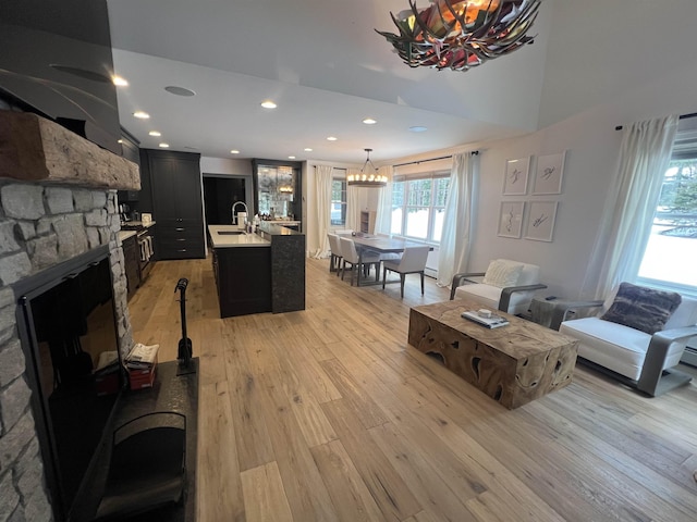 living room featuring a notable chandelier, a stone fireplace, recessed lighting, and light wood-style floors