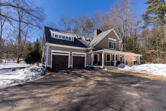 view of front of property with aphalt driveway, roof with shingles, a chimney, a porch, and a garage