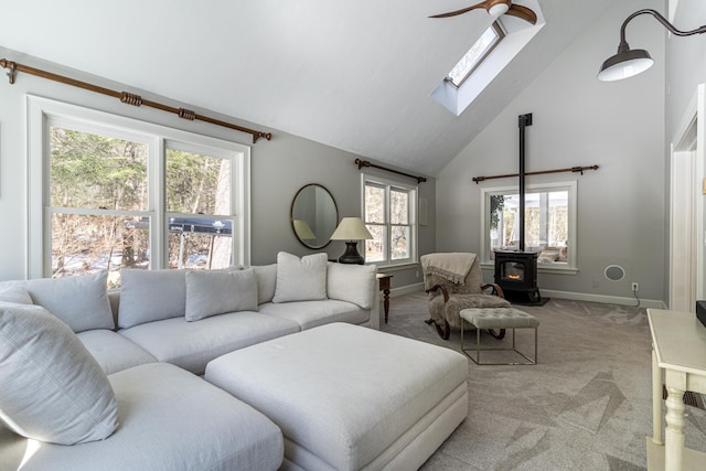 carpeted living room featuring high vaulted ceiling, a skylight, a ceiling fan, baseboards, and a wood stove