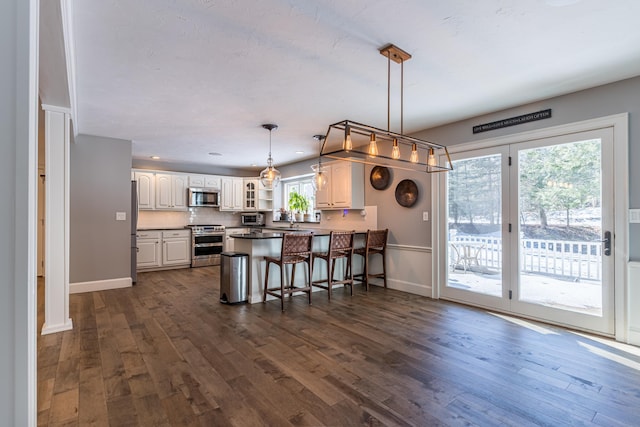 kitchen featuring dark wood finished floors, a breakfast bar, a peninsula, stainless steel appliances, and white cabinetry