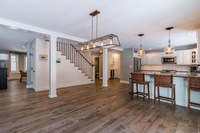 kitchen with dark countertops, appliances with stainless steel finishes, dark wood-type flooring, a kitchen bar, and white cabinetry