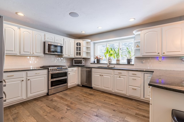 kitchen with dark countertops, appliances with stainless steel finishes, open shelves, and a sink