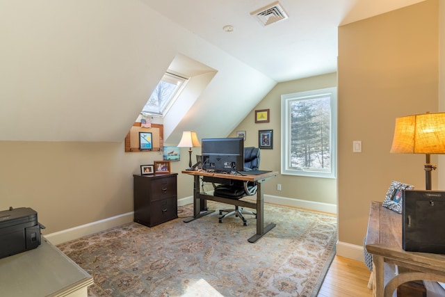 office with lofted ceiling with skylight, baseboards, visible vents, and wood finished floors