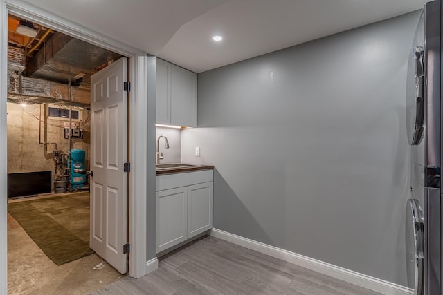 laundry area featuring recessed lighting, cabinet space, stacked washer / dryer, a sink, and baseboards