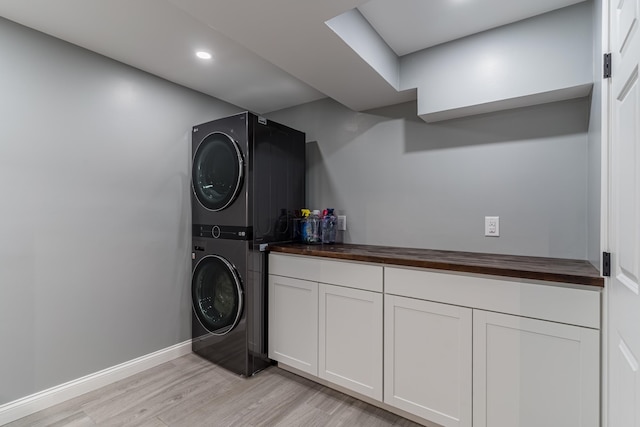 washroom featuring light wood finished floors, cabinet space, baseboards, stacked washer / drying machine, and recessed lighting