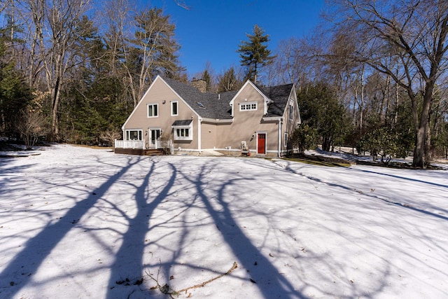 snow covered house with a chimney and a wooden deck