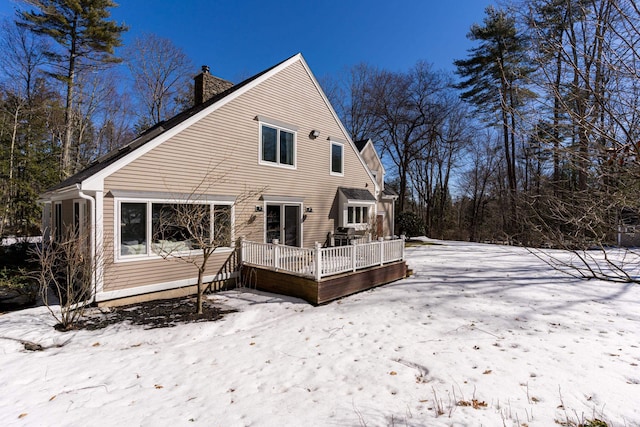 snow covered back of property with a chimney and a deck