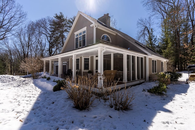 snow covered property featuring a sunroom and a chimney