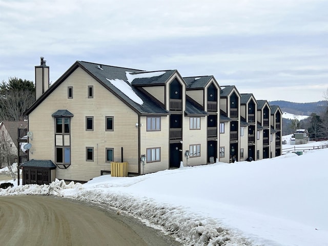 snow covered rear of property featuring a chimney