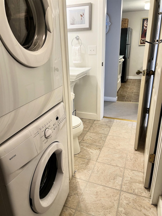 bathroom featuring stacked washer and clothes dryer, baseboards, and toilet