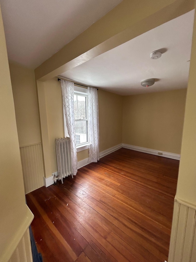 empty room featuring radiator, wood-type flooring, and wainscoting