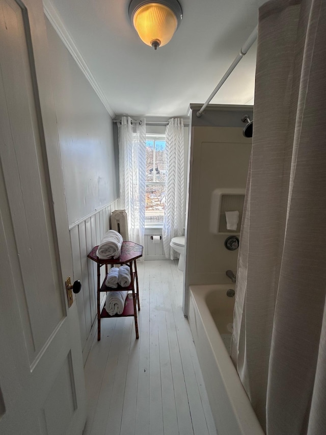 bathroom featuring toilet, a wainscoted wall, wood finished floors, shower / bath combo, and crown molding