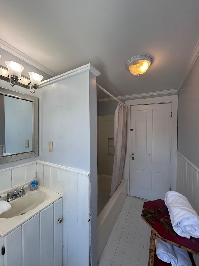 full bath with shower / tub combo, wood finished floors, vanity, ornamental molding, and wainscoting