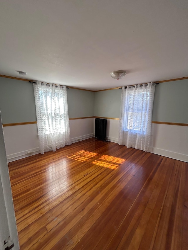 unfurnished living room with baseboards, crown molding, radiator heating unit, and hardwood / wood-style flooring