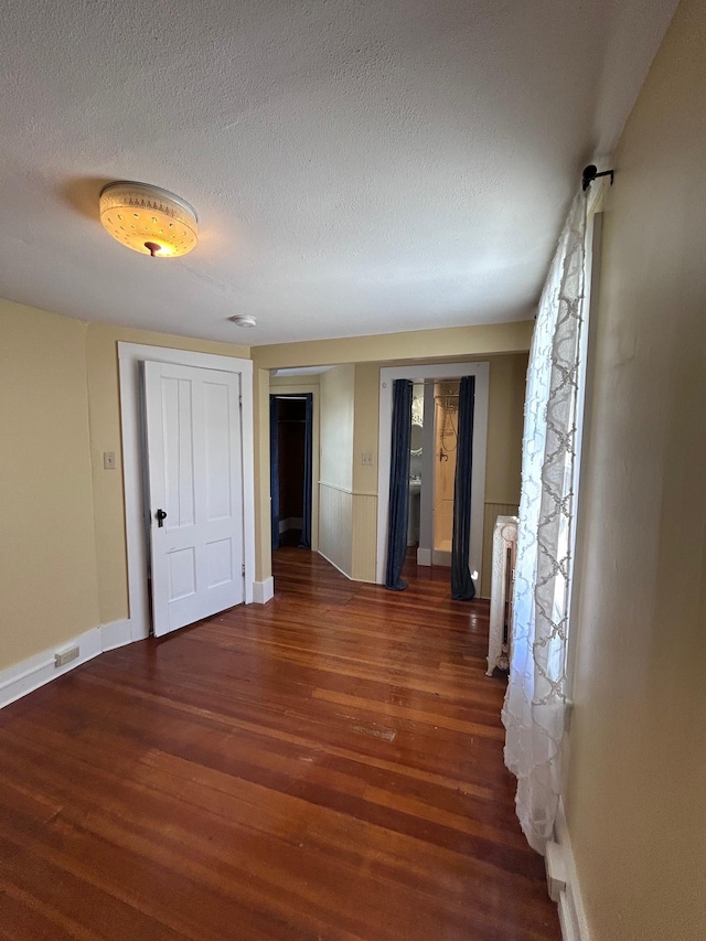 empty room with radiator, a textured ceiling, visible vents, and wood finished floors