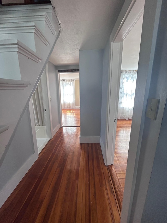 hall featuring a textured ceiling, baseboards, and dark wood-type flooring