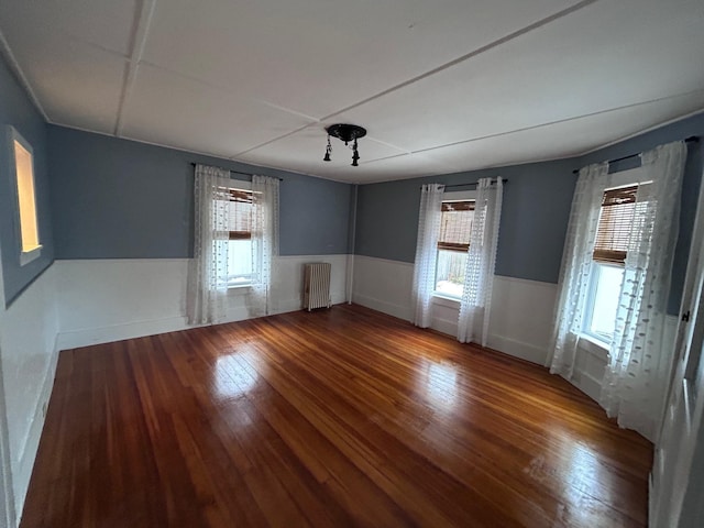 unfurnished room featuring radiator, a wainscoted wall, and hardwood / wood-style floors