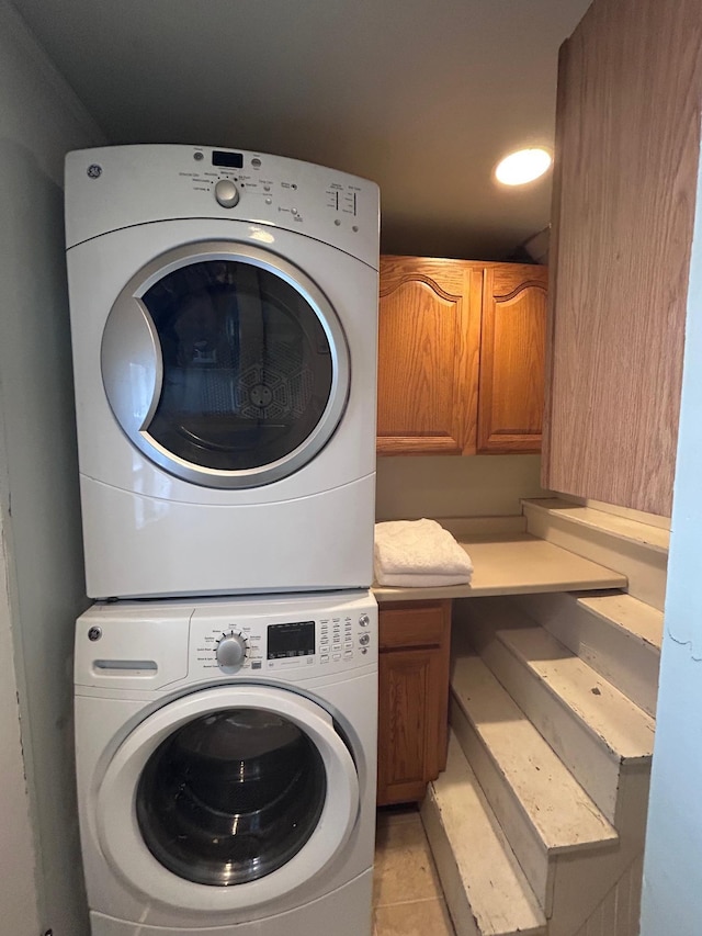 clothes washing area featuring cabinet space, light tile patterned floors, and stacked washer / dryer