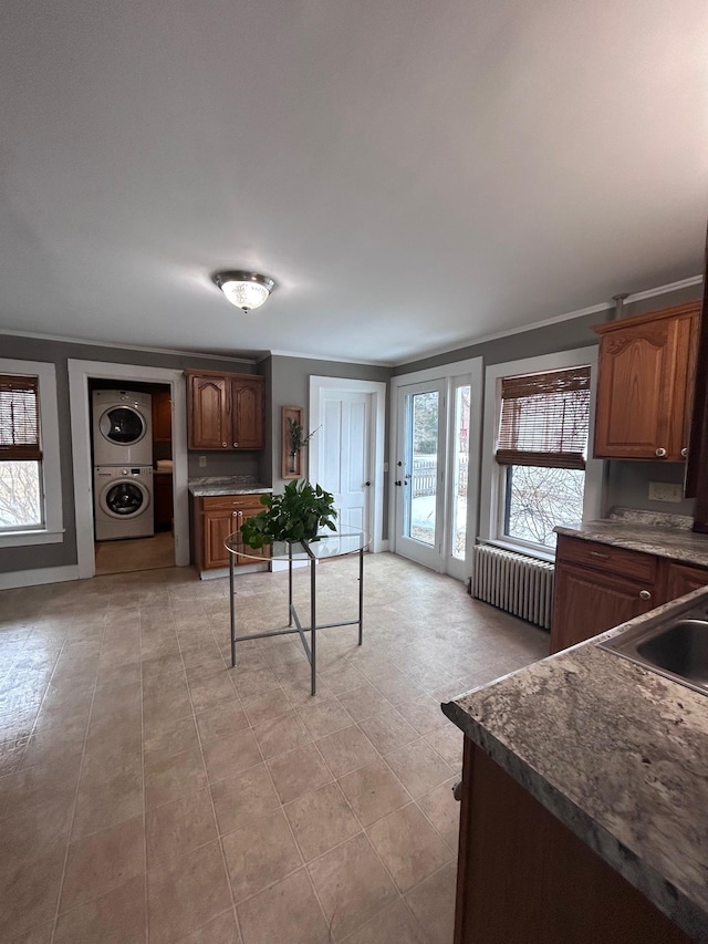 kitchen with radiator, crown molding, a sink, and stacked washer / drying machine