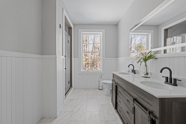 bathroom featuring a sink, a wainscoted wall, plenty of natural light, and toilet