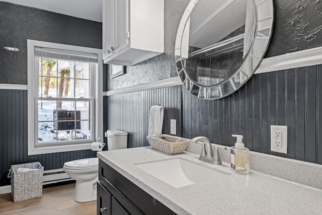 bathroom with vanity, wood finished floors, a wainscoted wall, a baseboard heating unit, and toilet