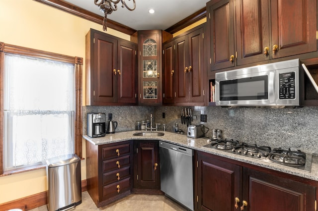 kitchen featuring light stone counters, stainless steel appliances, a sink, ornamental molding, and decorative backsplash