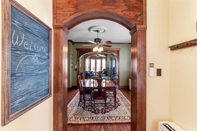 dining space with arched walkways, a ceiling fan, wood finished floors, crown molding, and a baseboard heating unit