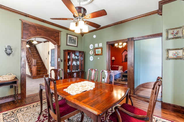 dining space featuring arched walkways, ceiling fan, wood finished floors, stairs, and crown molding