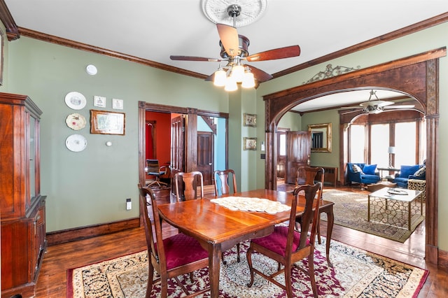 dining room featuring arched walkways, baseboards, ceiling fan, dark wood-type flooring, and crown molding