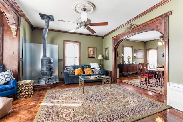 living area featuring arched walkways, ceiling fan, a wood stove, and a healthy amount of sunlight