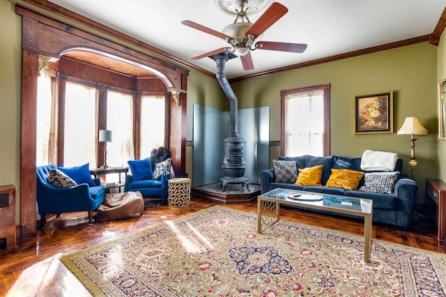 living area with ornamental molding, wood finished floors, a wood stove, and a ceiling fan