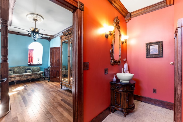 bathroom featuring ceiling fan, wood finished floors, vanity, baseboards, and ornamental molding