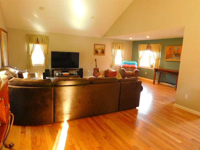 living area featuring high vaulted ceiling, light wood-type flooring, plenty of natural light, and baseboards