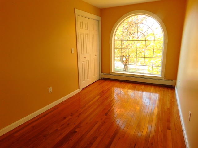 unfurnished room featuring a baseboard heating unit, hardwood / wood-style flooring, and baseboards