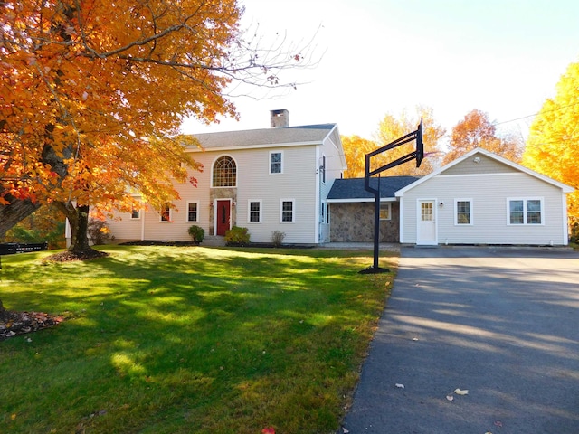 view of front facade with driveway, a front lawn, a chimney, and stone siding