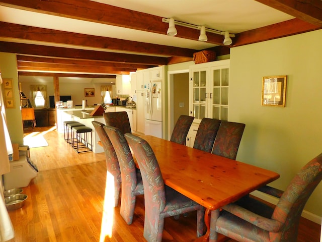 dining space featuring light wood finished floors, beam ceiling, and rail lighting