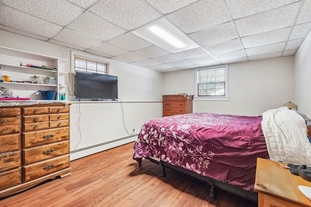 bedroom featuring light wood finished floors, a baseboard heating unit, and a drop ceiling