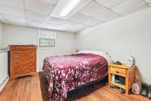 bedroom featuring a baseboard heating unit, a paneled ceiling, and wood finished floors