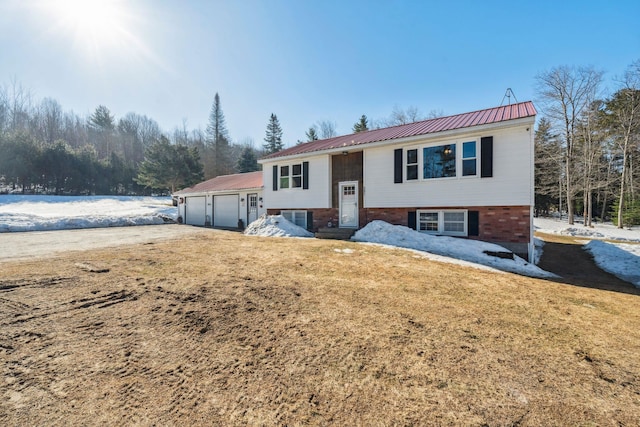 split foyer home featuring an attached garage, a front yard, metal roof, and brick siding