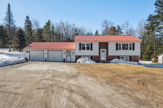 split foyer home featuring dirt driveway, metal roof, and a garage