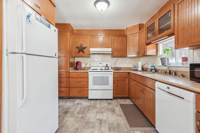 kitchen with white appliances, brown cabinetry, light countertops, under cabinet range hood, and a sink