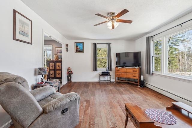 living room featuring a baseboard heating unit, wood-type flooring, a healthy amount of sunlight, and ceiling fan