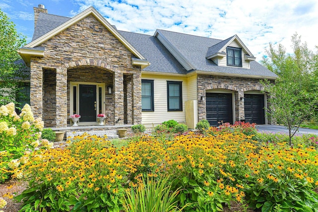 view of front of property featuring a shingled roof, stone siding, driveway, and a garage