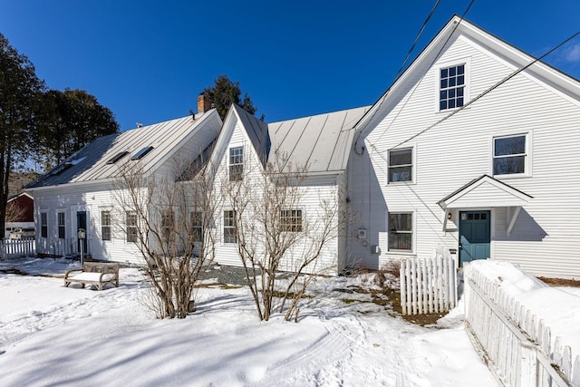 view of front facade featuring a standing seam roof, fence, a chimney, and metal roof