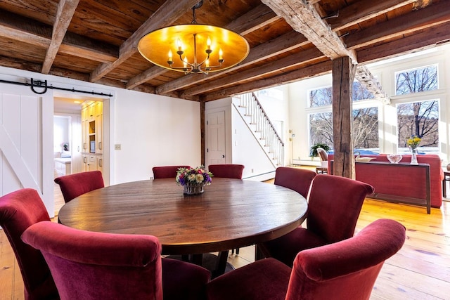 dining room featuring beam ceiling, an inviting chandelier, a barn door, wood ceiling, and stairs