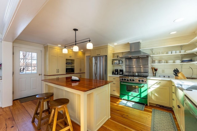 kitchen with stainless steel appliances, tasteful backsplash, butcher block counters, light wood-style floors, and wall chimney range hood