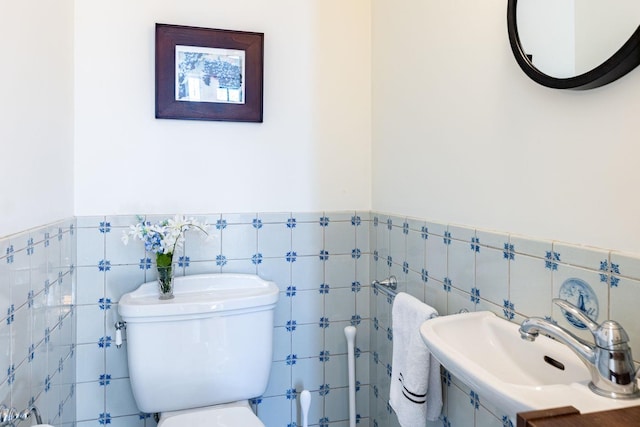 half bathroom with wainscoting, a sink, tile walls, and toilet