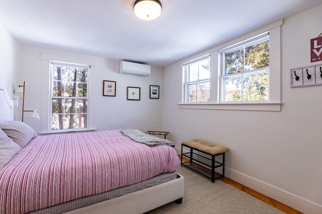 bedroom with an AC wall unit, multiple windows, baseboards, and wood finished floors