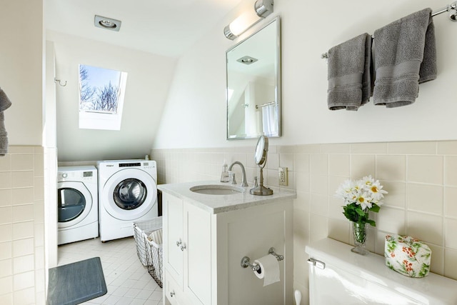 laundry room featuring washing machine and dryer, a wainscoted wall, laundry area, a sink, and tile walls